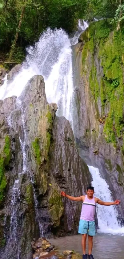 Man in front of a stunning waterfall in a lush green forest.