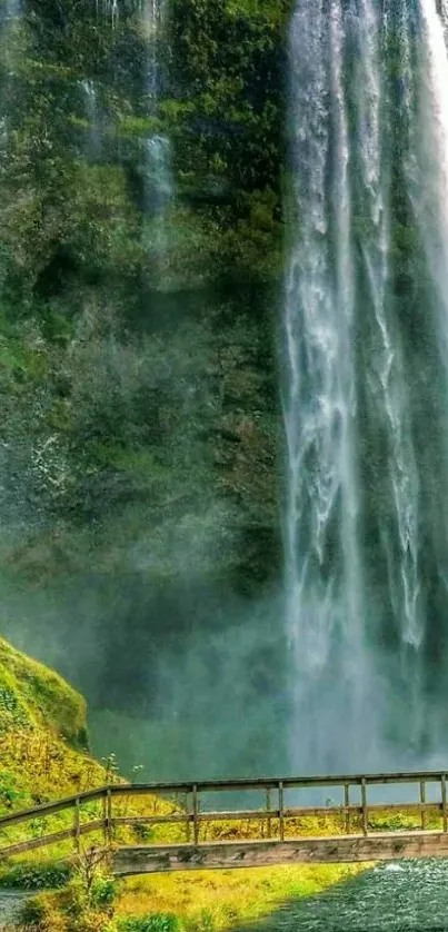 Majestic waterfall flowing over lush green landscape with a wooden bridge.