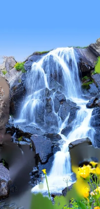 Vibrant waterfall over rocks with flowers and blue sky.