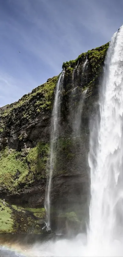 Mobile wallpaper of a majestic waterfall cascading over a lush green cliff under a blue sky.