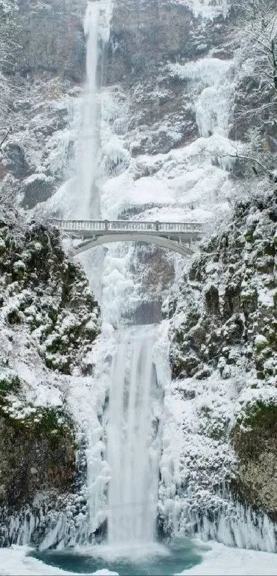 Majestic waterfall with snow-covered landscape and bridge in winter.