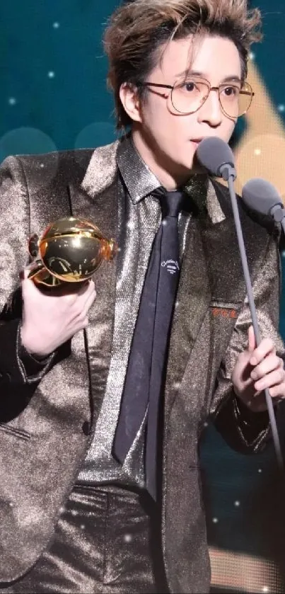 Stylish person in shiny suit holding a trophy with a blue backdrop.