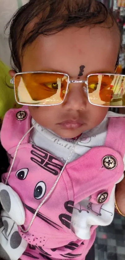 Adorable baby in pink dungarees wearing sunglasses in a busy market.