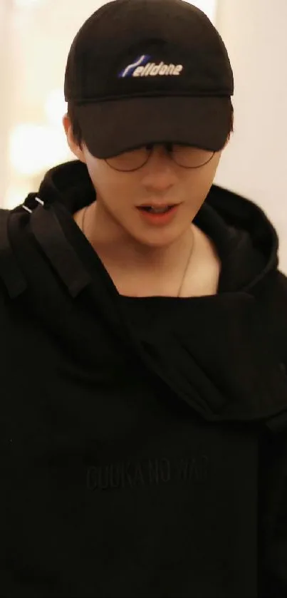 Person in black hoodie with glasses and cap, stylish vibe.