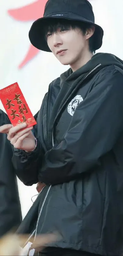 Person in a black jacket holding a red envelope.