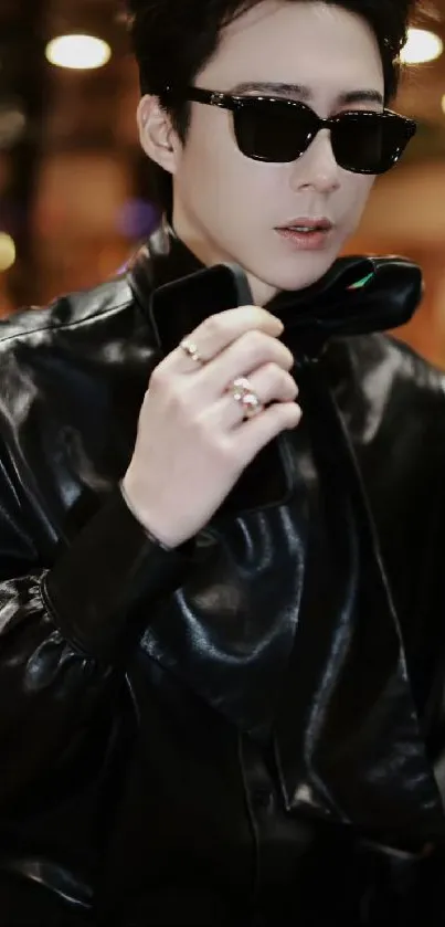 Person in black leather jacket holding a phone, showcasing stylish fashion.