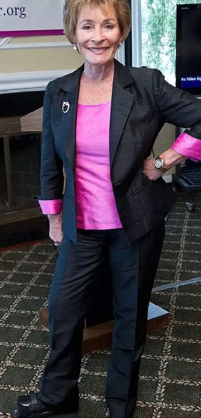 Woman in a black suit with pink accents poses on a patterned carpet.