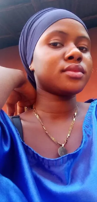 Woman in a blue dress with matching head wrap poses elegantly.