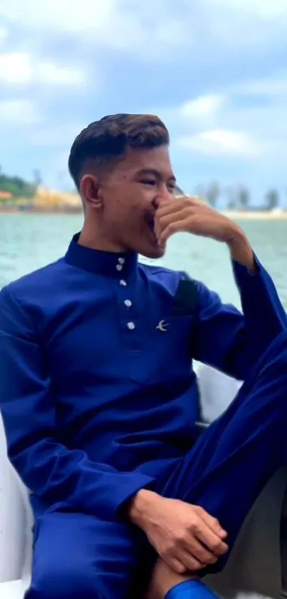 Man in blue outfit relaxing on a boat against a scenic lake background.