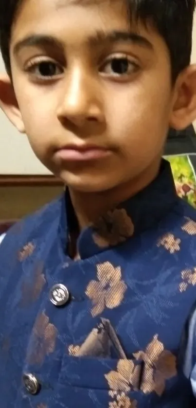 A young boy in a stylish blue floral jacket posing indoors.