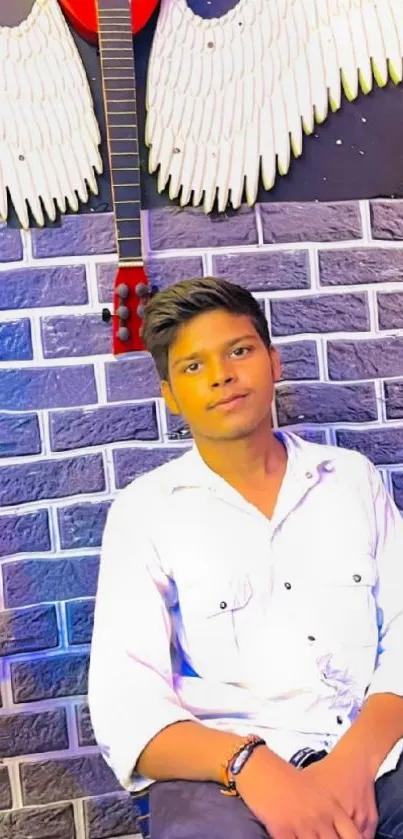 Young man against brick wall with angel wings and guitar.