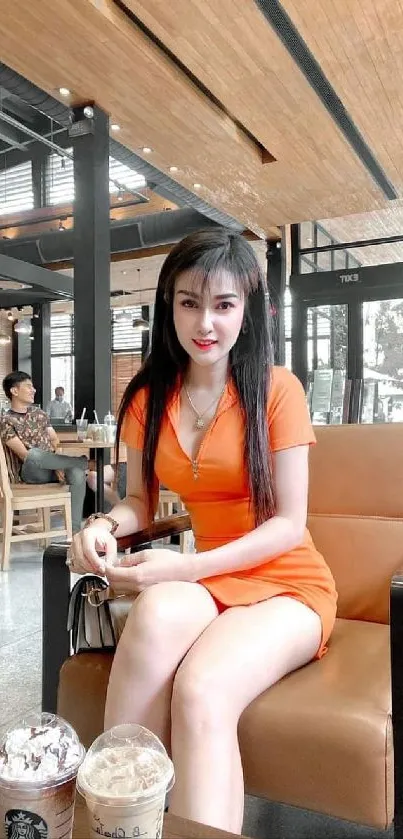 Woman in an orange dress sitting in a stylish cafe setting.