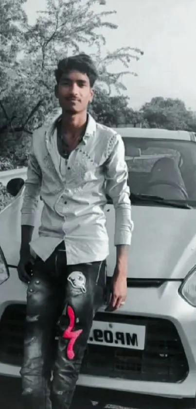 Young man posing with car in scenic grayscale setting.