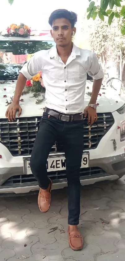 Man in white shirt leaning on decorated car under green trees.