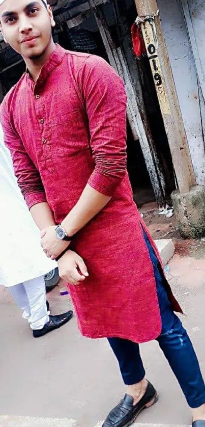 Man in maroon kurta and blue jeans standing outdoors.