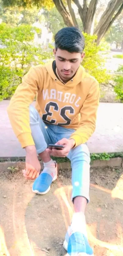 Young man in casual hoodie seated outdoors on phone.