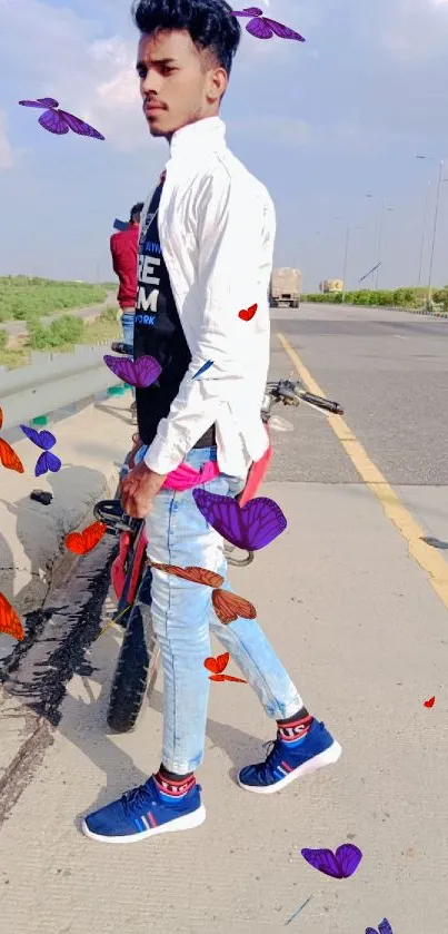 Young man in casual attire stands on a sunny road with a bike.