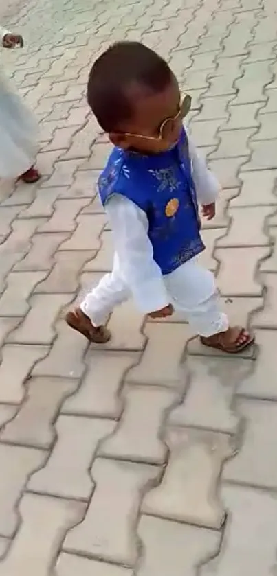 Young child wearing a blue vest and sunglasses walking on a paved street.