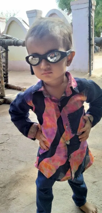 Child wearing sunglasses in a rustic village setting.