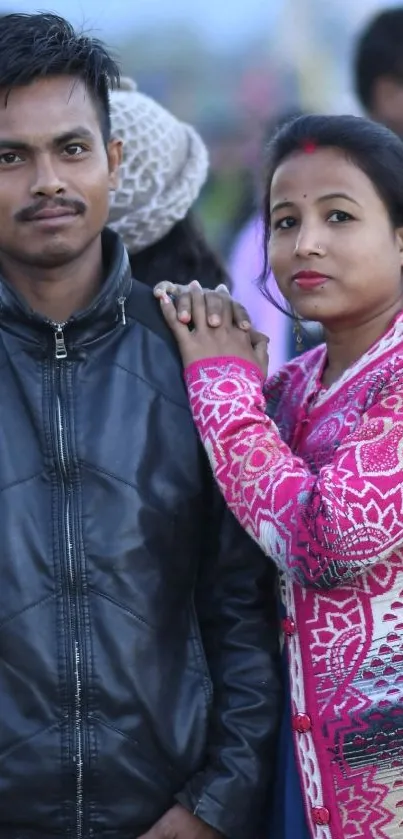 A couple posing outdoors, man in leather jacket, woman in pink design.