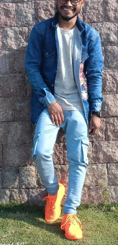 Man in stylish denim with orange shoes against a stone wall.