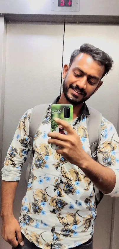 Modern elevator selfie with floral shirt and smartphone reflection.