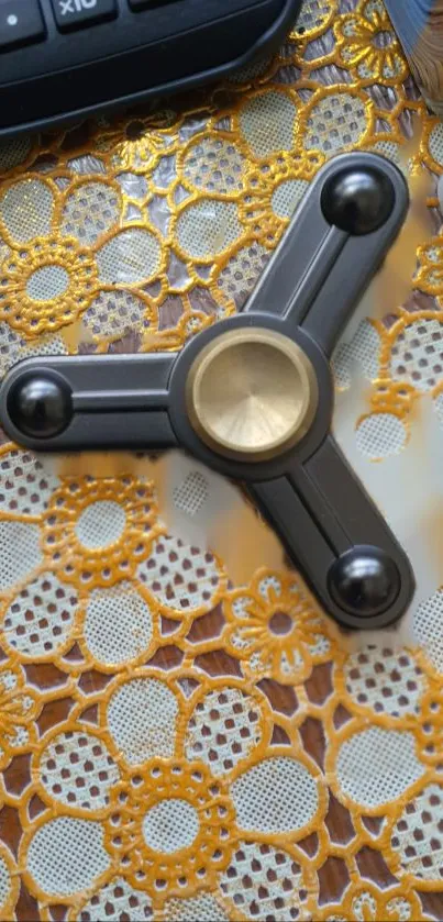 Black and gold fidget spinner on lace-patterned background.