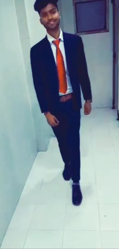 Young man in formal attire with orange tie walking in hallway.