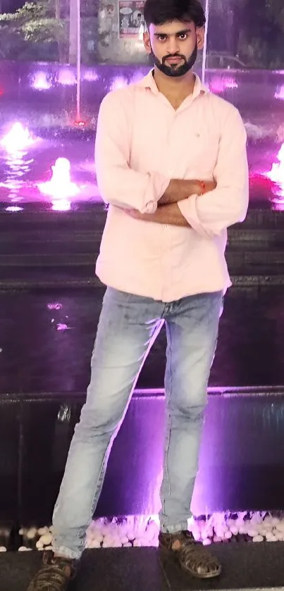 Person standing by a colorful, illuminated fountain at night.