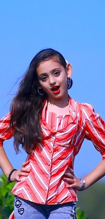 Stylish young girl in a red top posing against a clear blue sky.