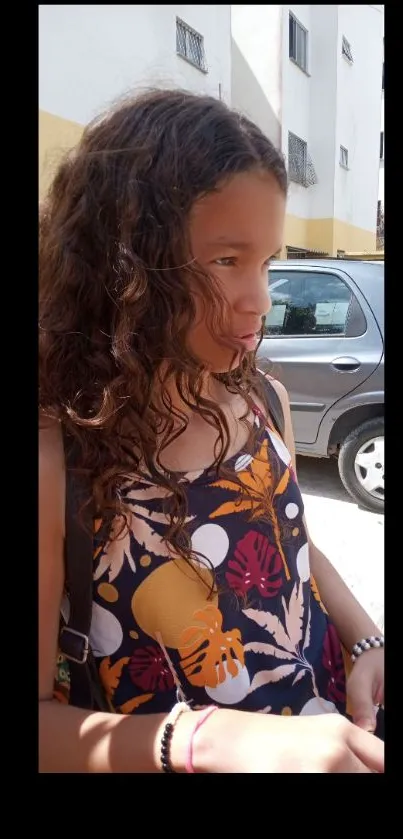 Young girl with curly hair and a colorful outfit in an urban setting.