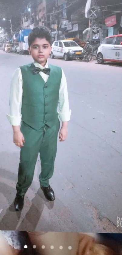 Boy in green suit standing on a lit city street at night.
