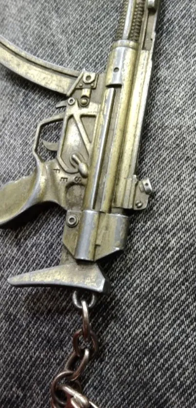 Silver gun keychain on gray denim background.