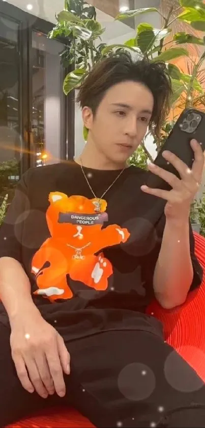 Man in black shirt with orange print sitting on red chair using smartphone.