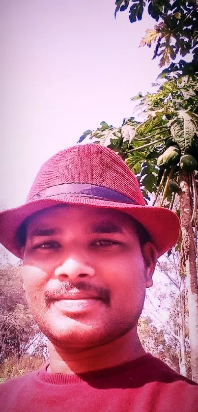 Man in red hat with greenery background and pink hues.