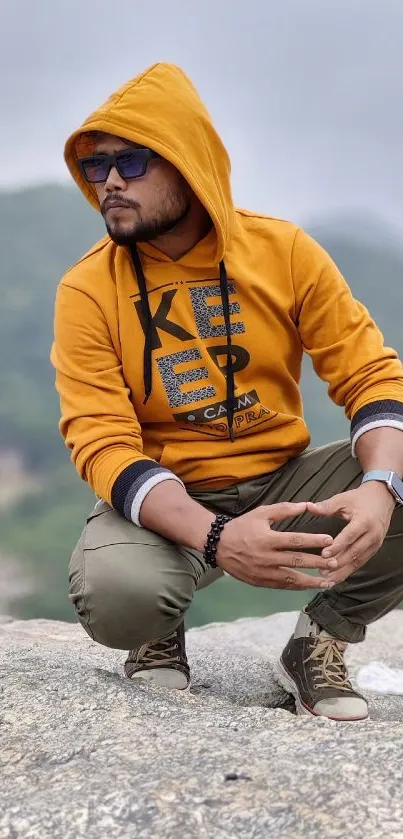 Person in orange hoodie posing on rocky surface outdoors.