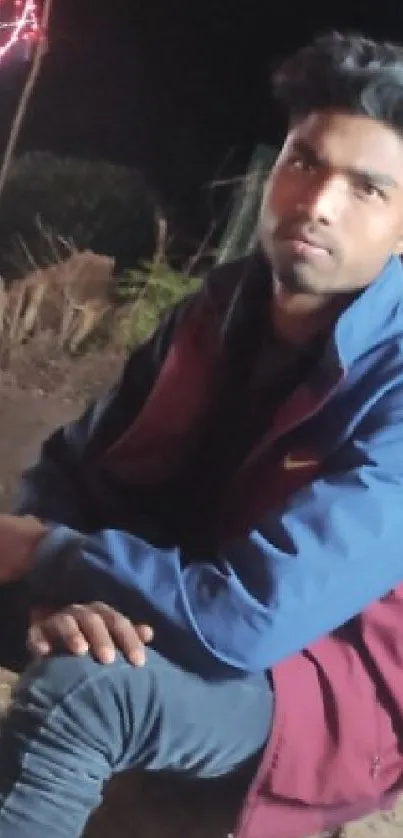 Person in blue and red jacket sitting outdoors at night.