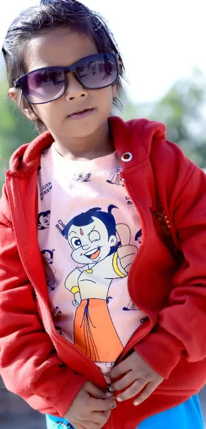 Kid in red jacket and sunglasses with cartoon t-shirt.