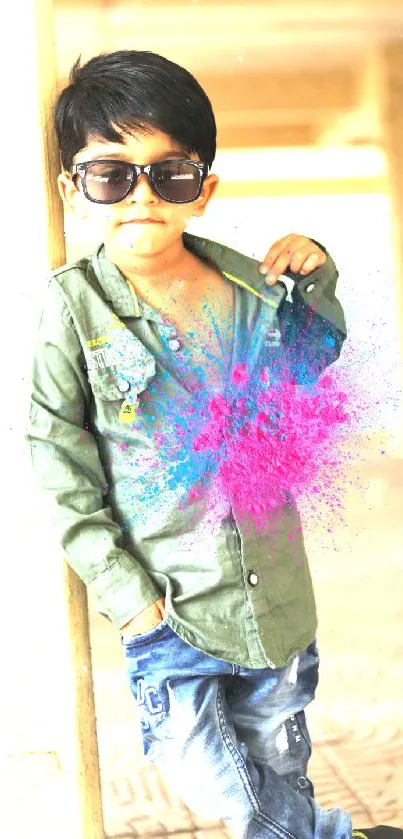 Boy with sunglasses stands against a colorful splash effect on a sunny day.