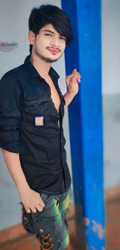 Stylish young man in casual fashion leaning against blue wall.