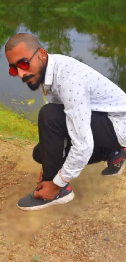 Man crouching by riverside with casual fashion style.