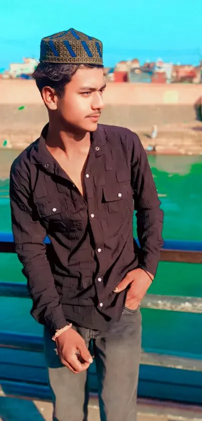 Man in black shirt standing by a river with a sky blue background.