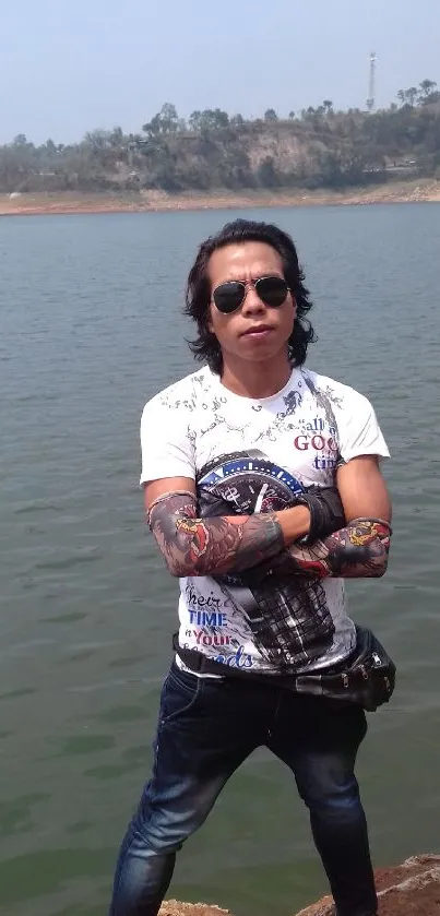 Man with tattoos by a serene blue lake.