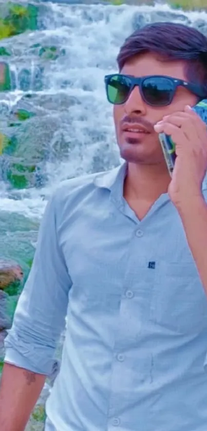 Man in sunglasses talking on phone by a stunning waterfall.