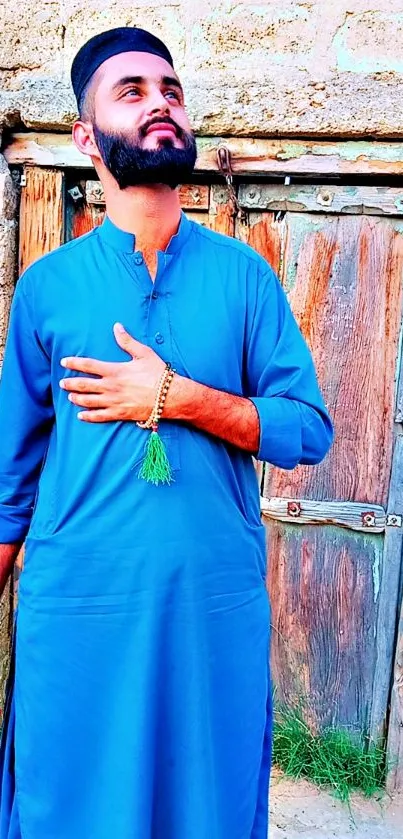 Man in traditional blue outfit standing by rustic wooden door.