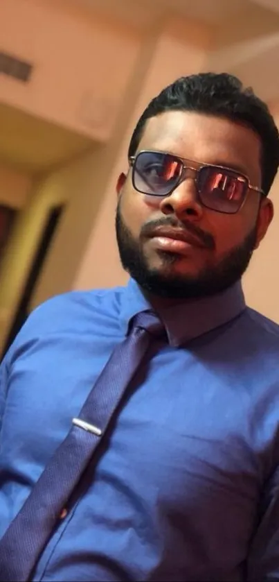 A stylish man wearing a blue shirt and glasses in an indoor setting.