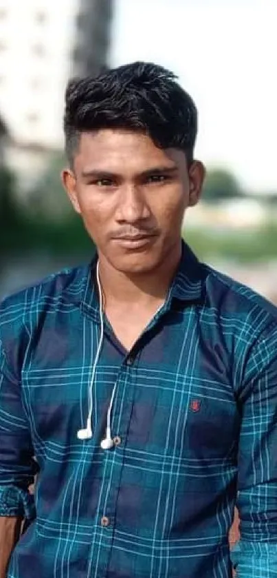 Confident man in blue plaid shirt with earphones against urban backdrop.