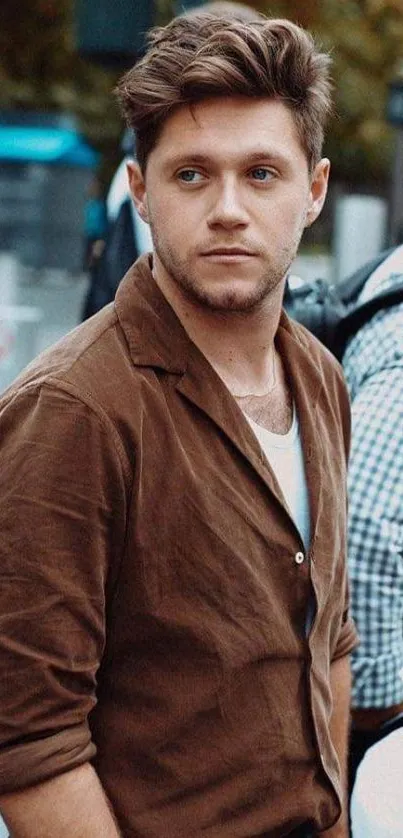 Man in a brown shirt posing outdoors, stylish and elegant.