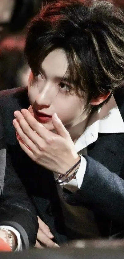 Man in black suit with hand near face, stylish portrait.