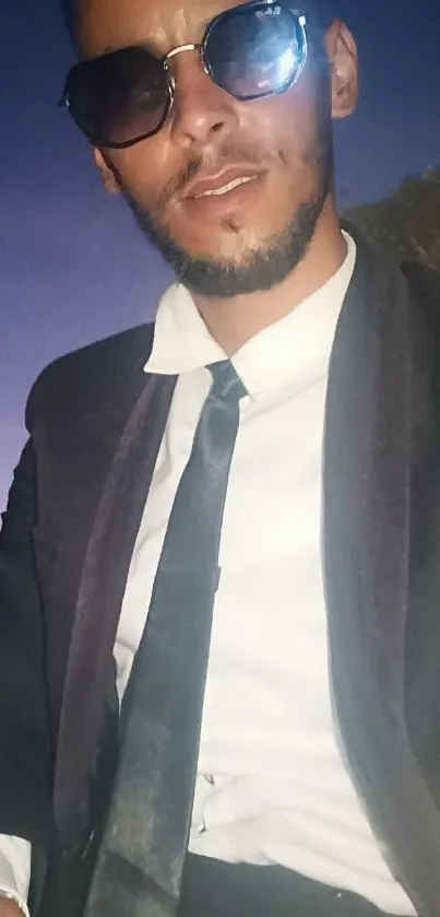 Man in formal suit with sunglasses under a twilight sky.